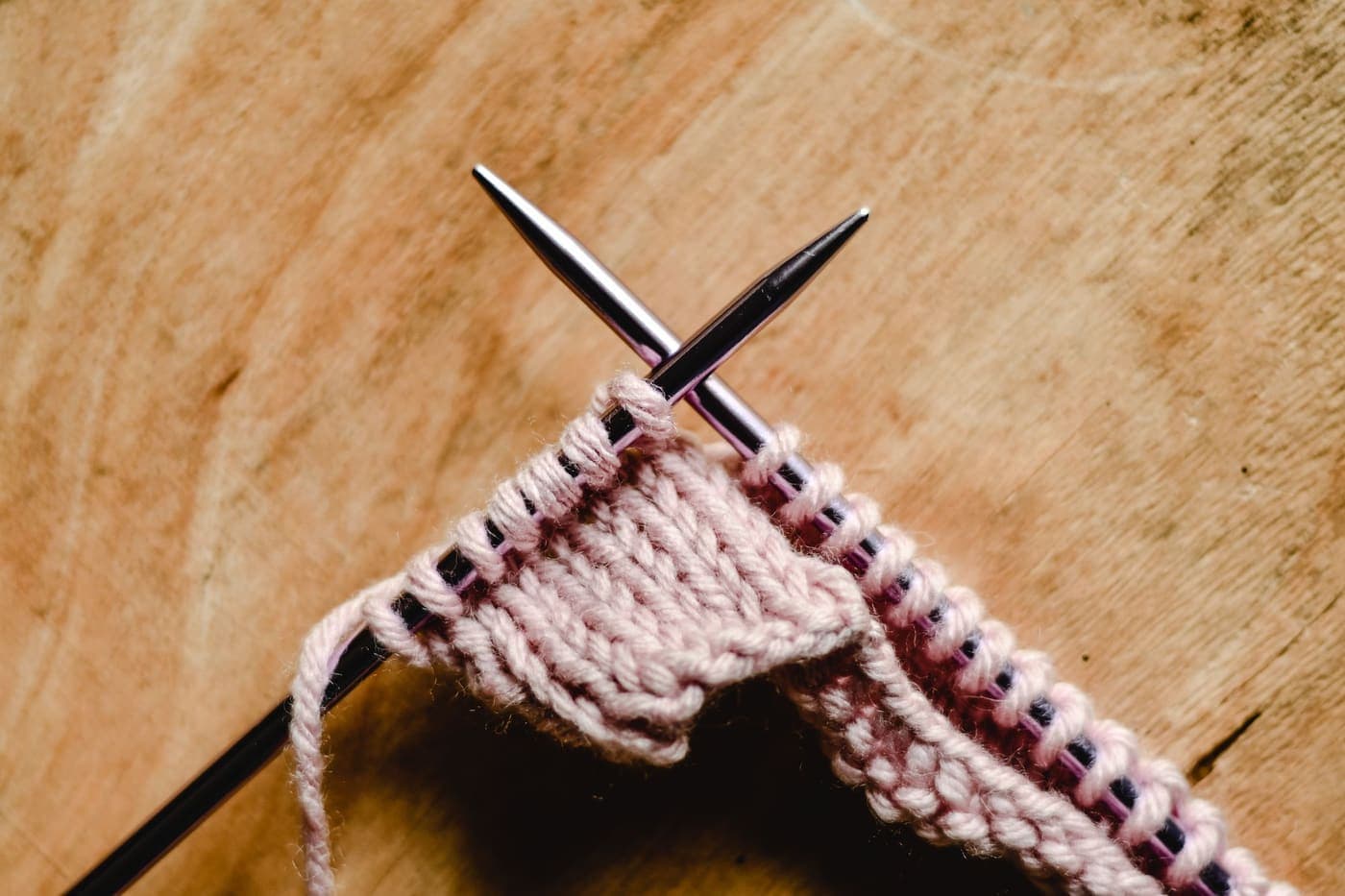 Close-up of knitting needles with pink yarn on a wooden surface