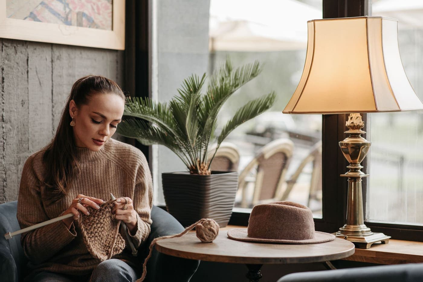 A woman knitting indoors beside a warm lamp