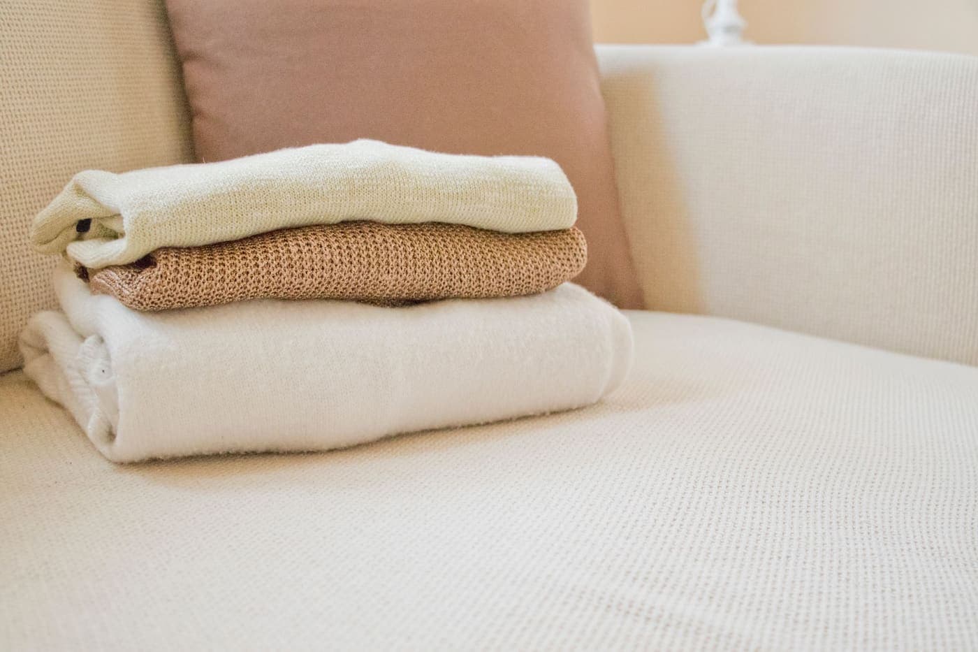 Soft folded sweaters in warm tones on a cream sofa