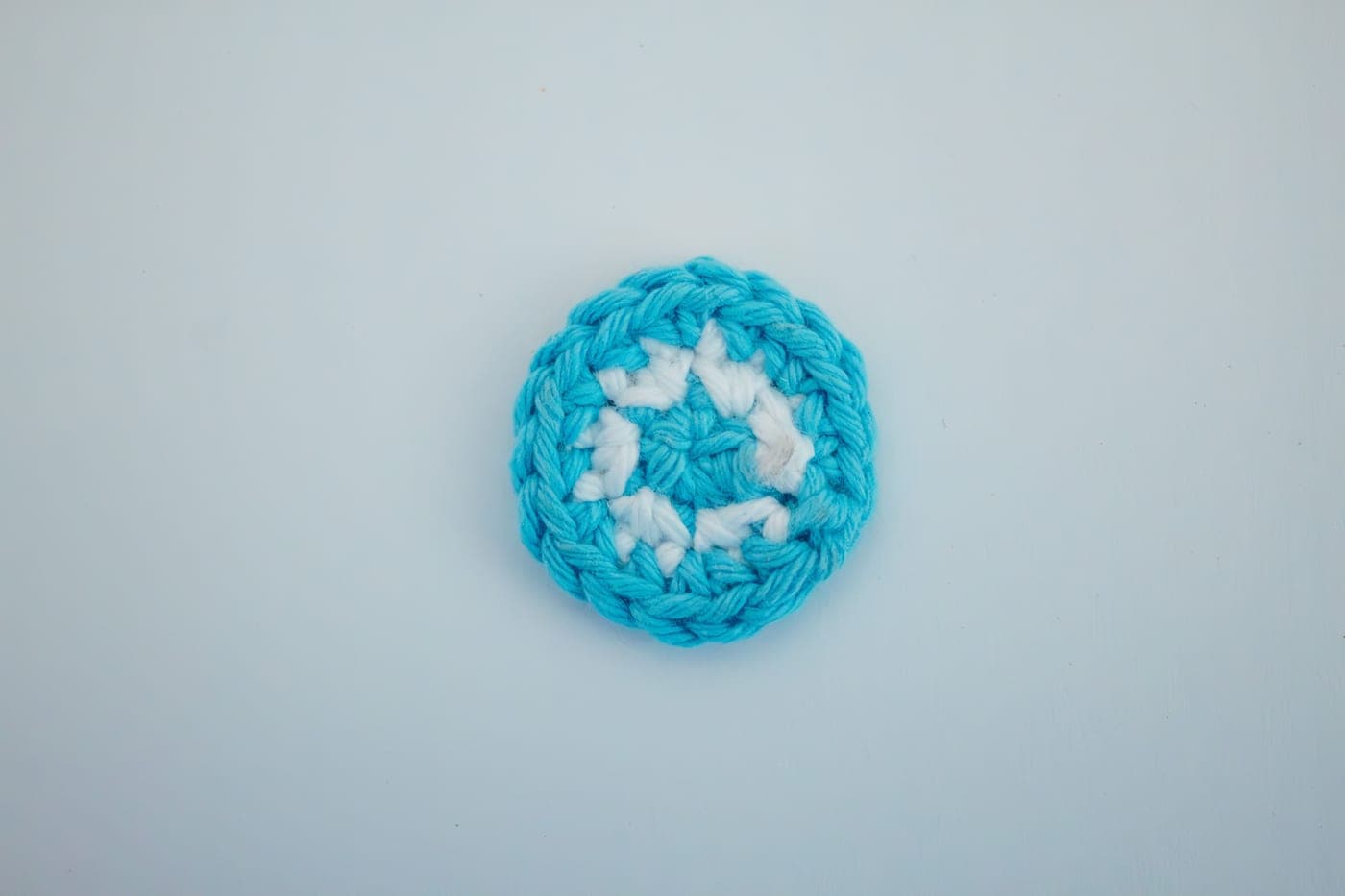 A bottle of fabric adhesive beside yarn and a finished crochet piece