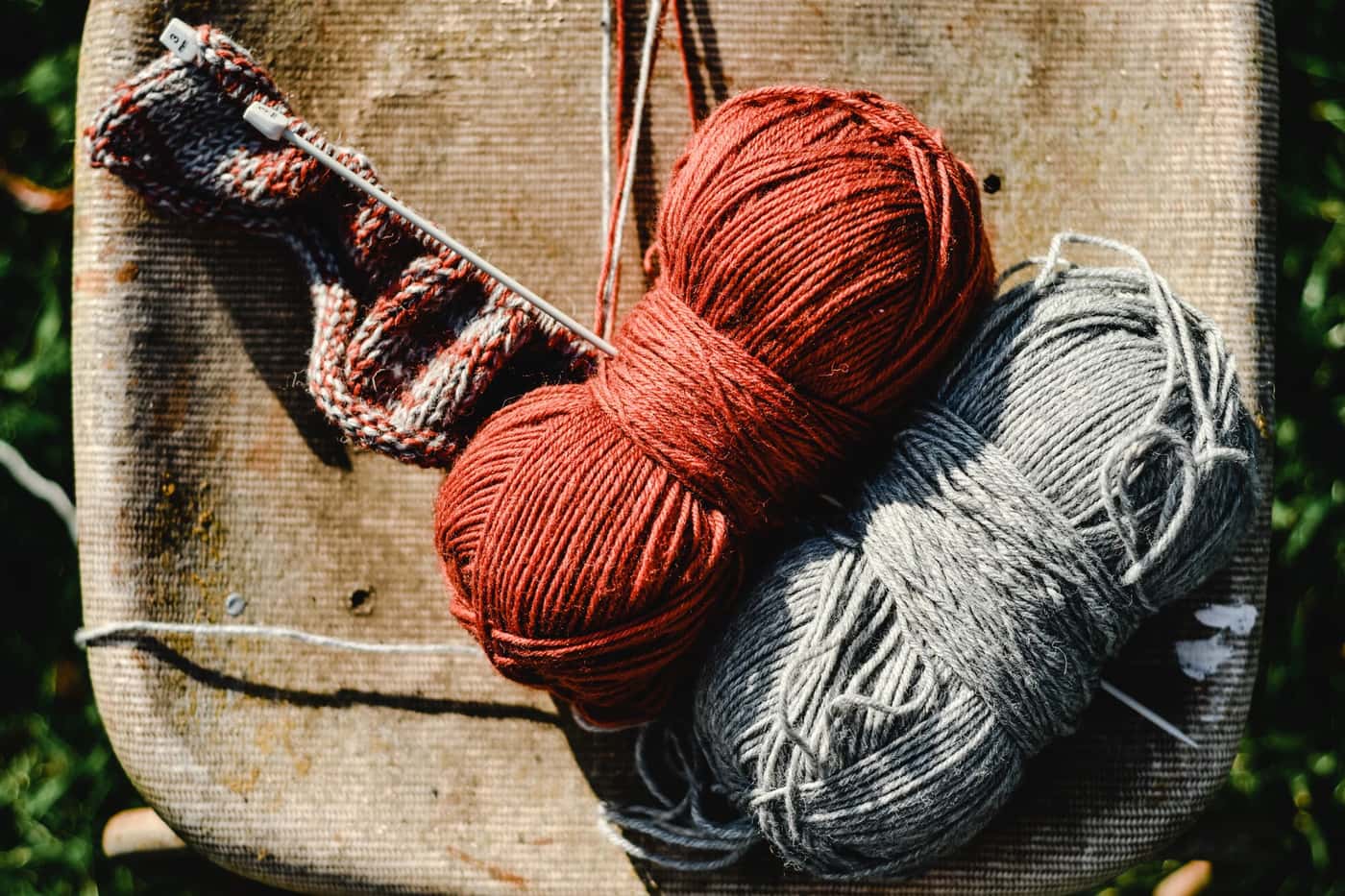 Balls of red and gray yarn with knitting needles on a rustic wooden chair