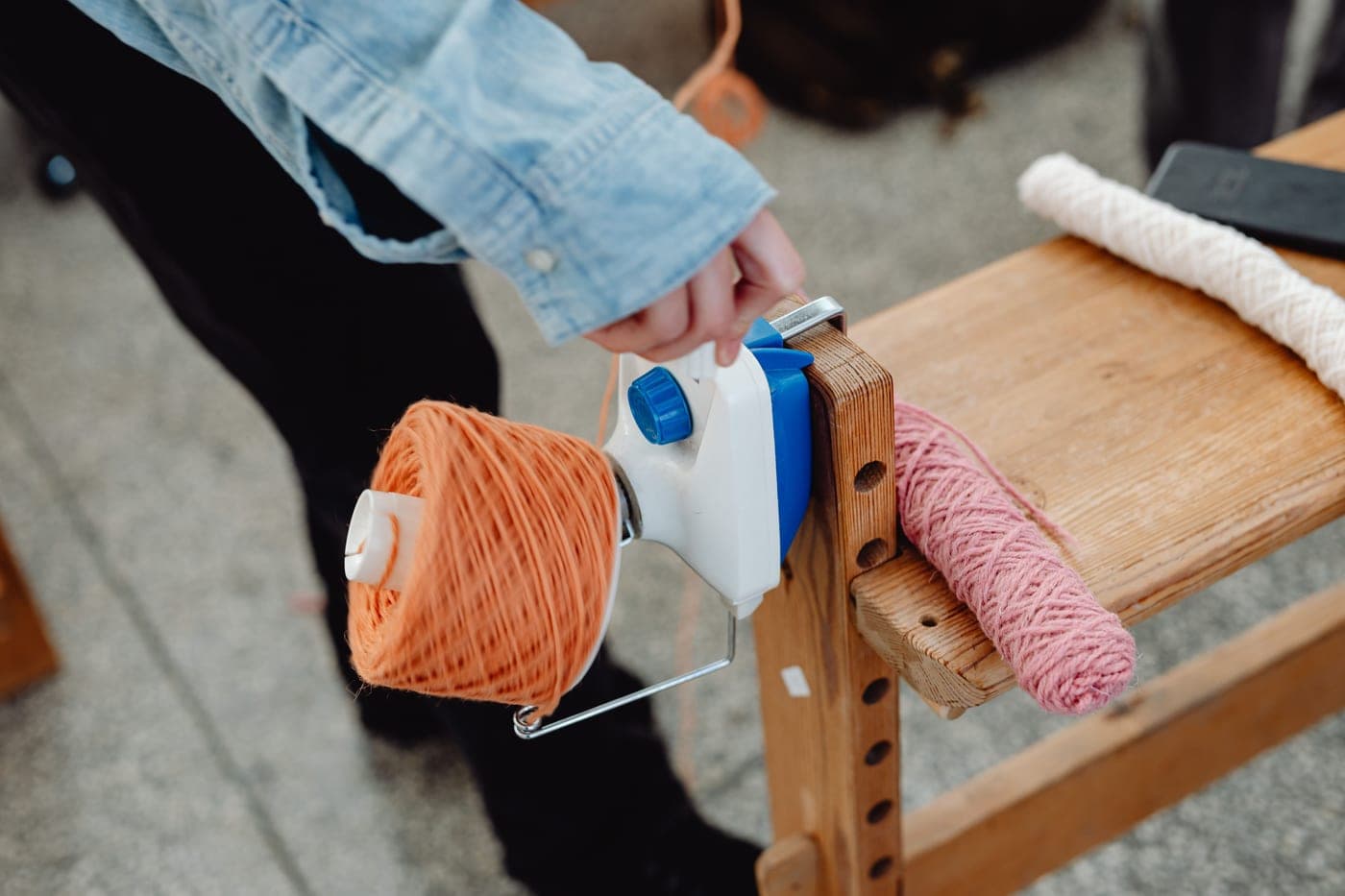 A hand-cranked yarn ball winder clamped to a table with a cake of yarn on it