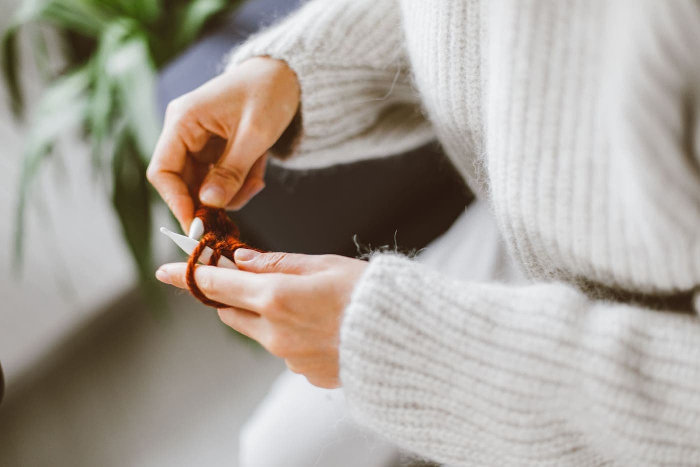 A person in a white knitted sweater knitting