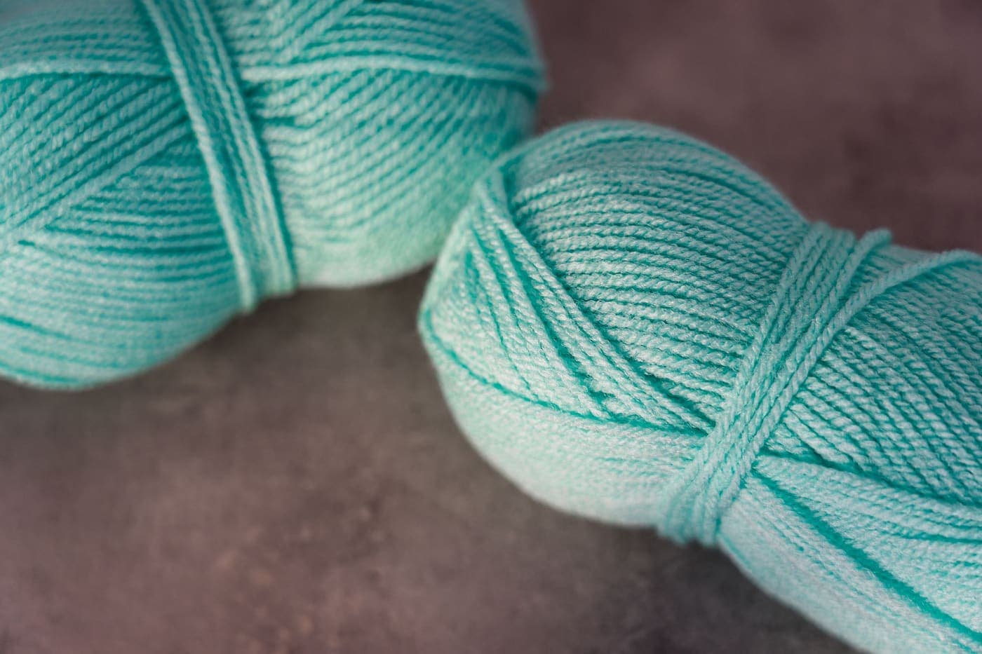 Two turquoise balls of yarn resting on a textured surface