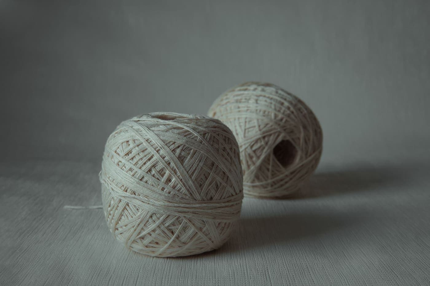 Two balls of natural undyed yarn on a plain background