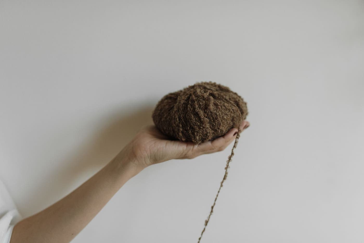 A hand holding a ball of soft brown mohair yarn