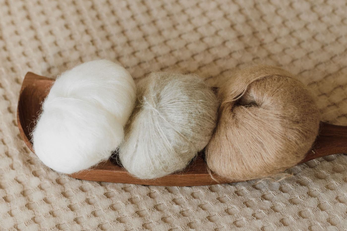 Three balls of wool yarn in neutral tones on a wooden tray