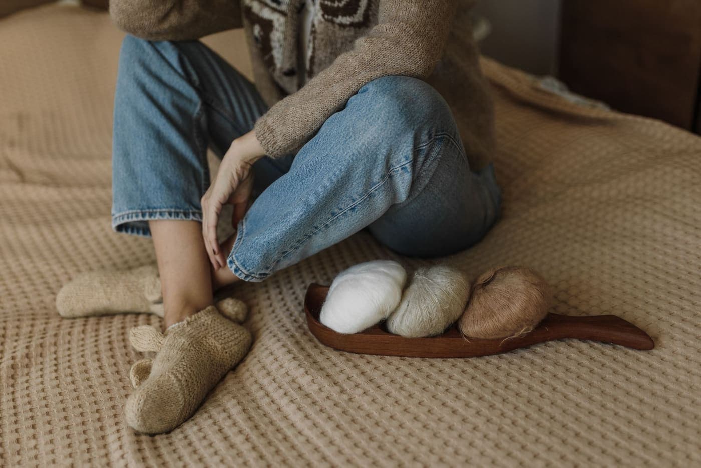 A person sitting with balls of yarn and knitted slippers on a bed