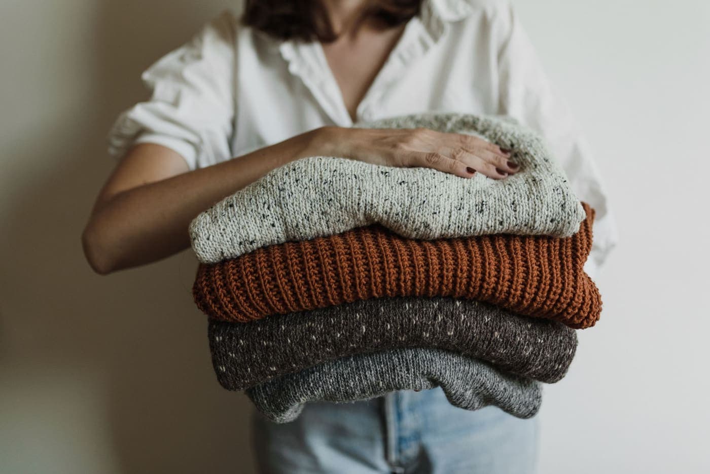 A person holding a stack of folded knitted sweaters