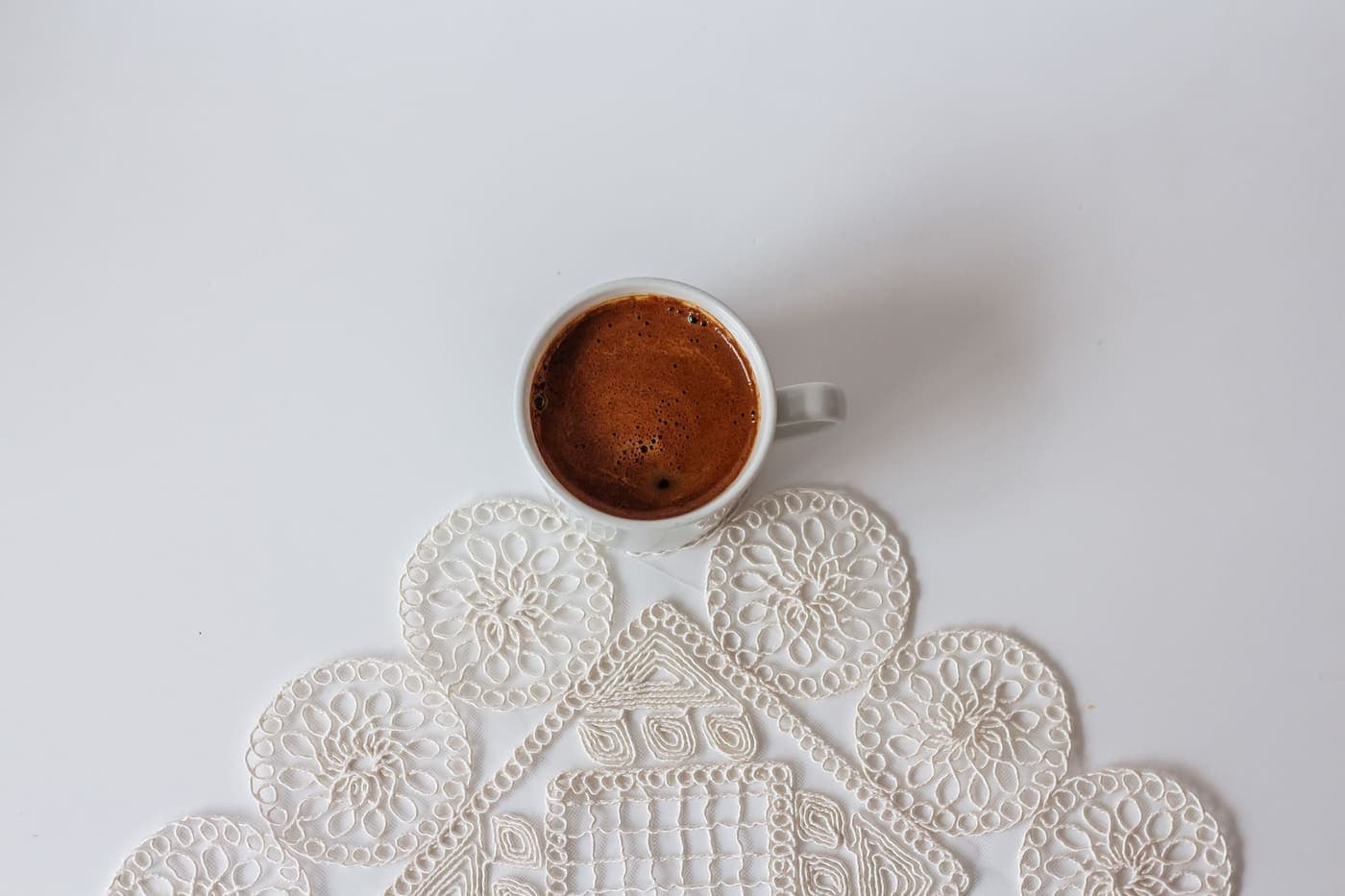 A white coffee cup resting on a crochet doily