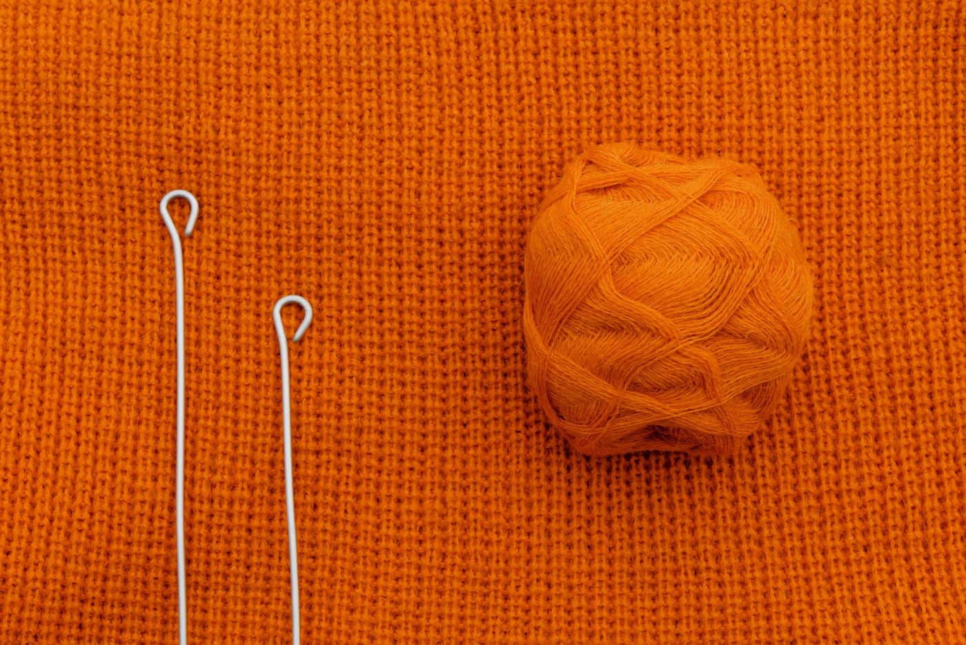A ball of orange yarn resting on knitted fabric with metal needles