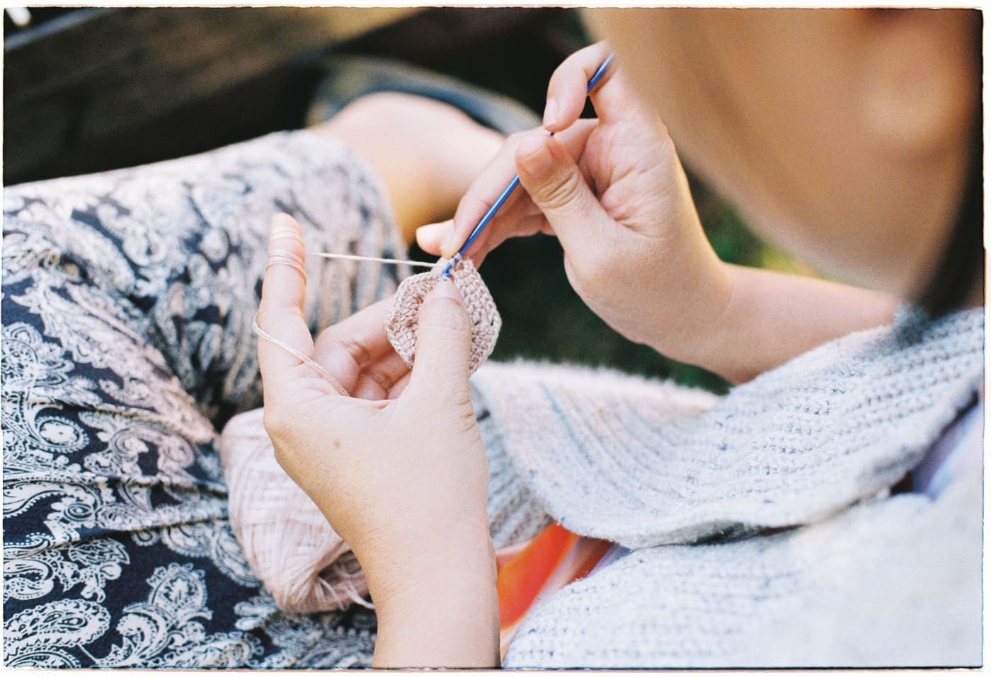 A person crocheting outdoors, hook and yarn in close focus