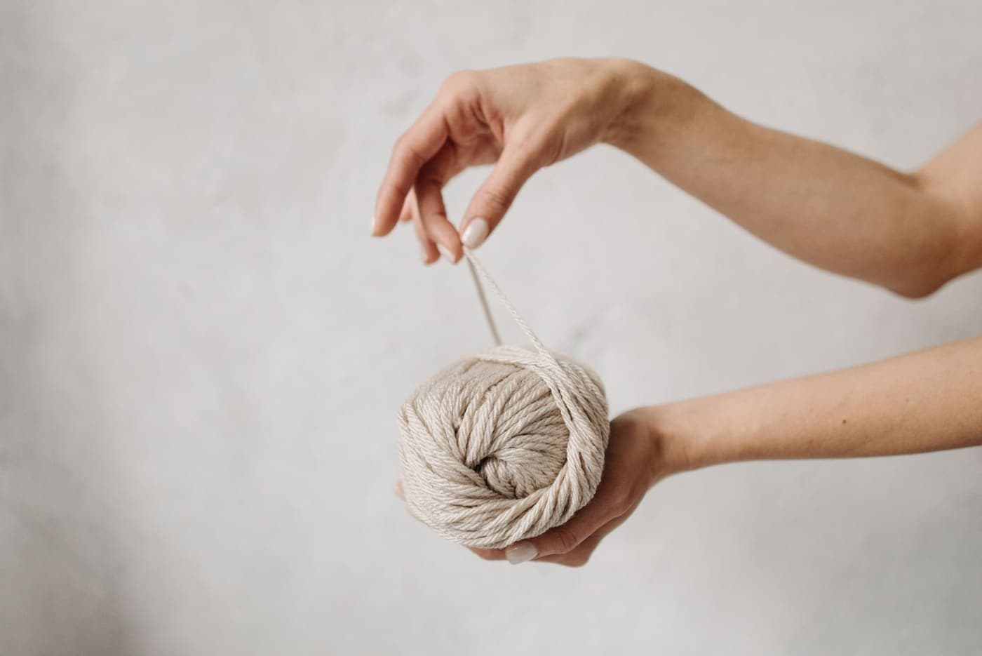 A hand holding a ball of beige yarn