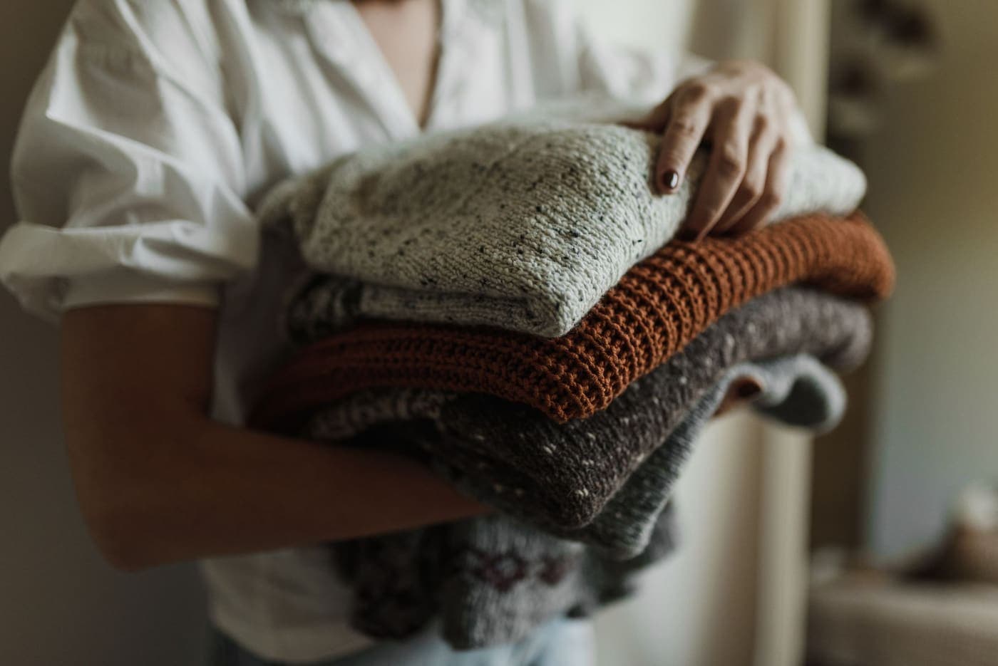 A person holding a stack of folded knitted sweaters in autumn colors