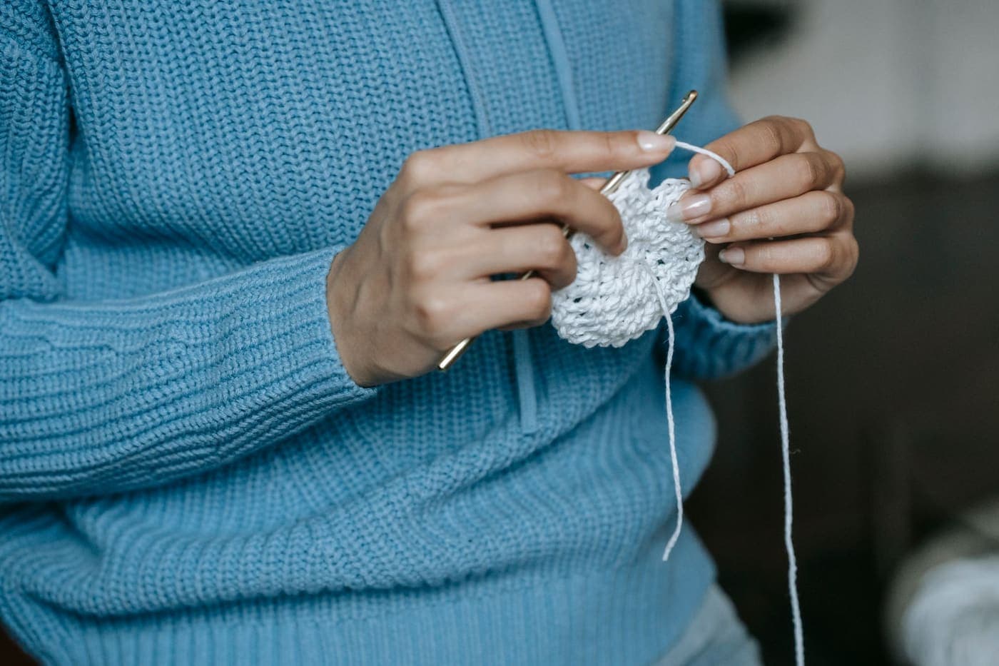 Hands working a white crochet piece with a metal hook