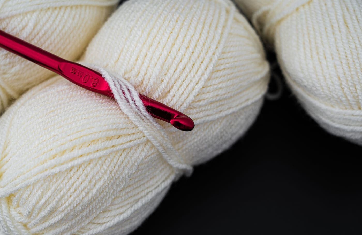 Cream colored yarn balls beside a red crochet hook in close-up