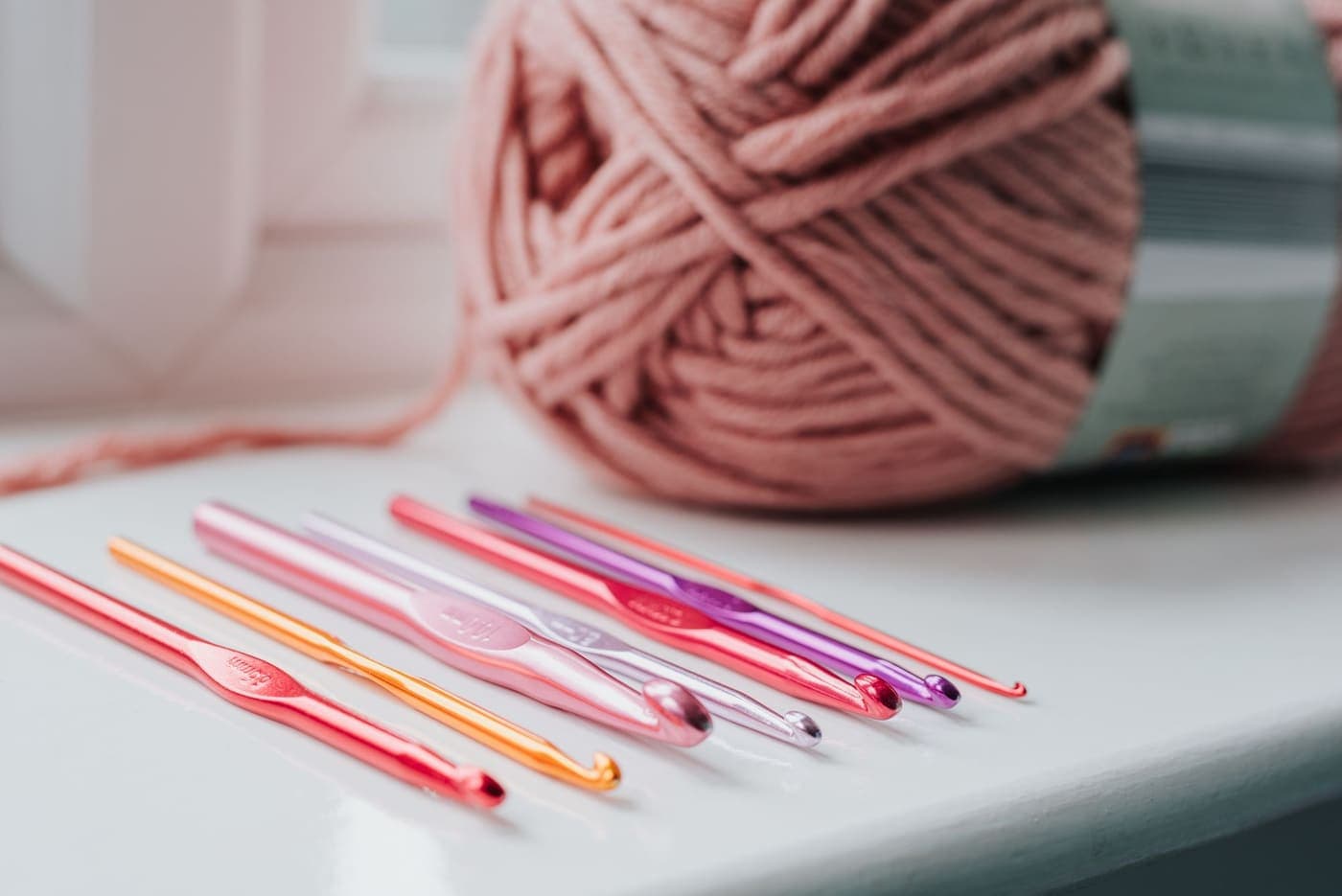 A row of multicolored crochet hooks beside a ball of beige yarn