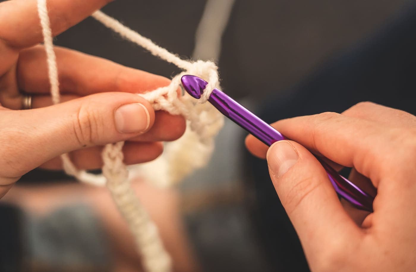 Hands crocheting cream-colored yarn with a purple hook