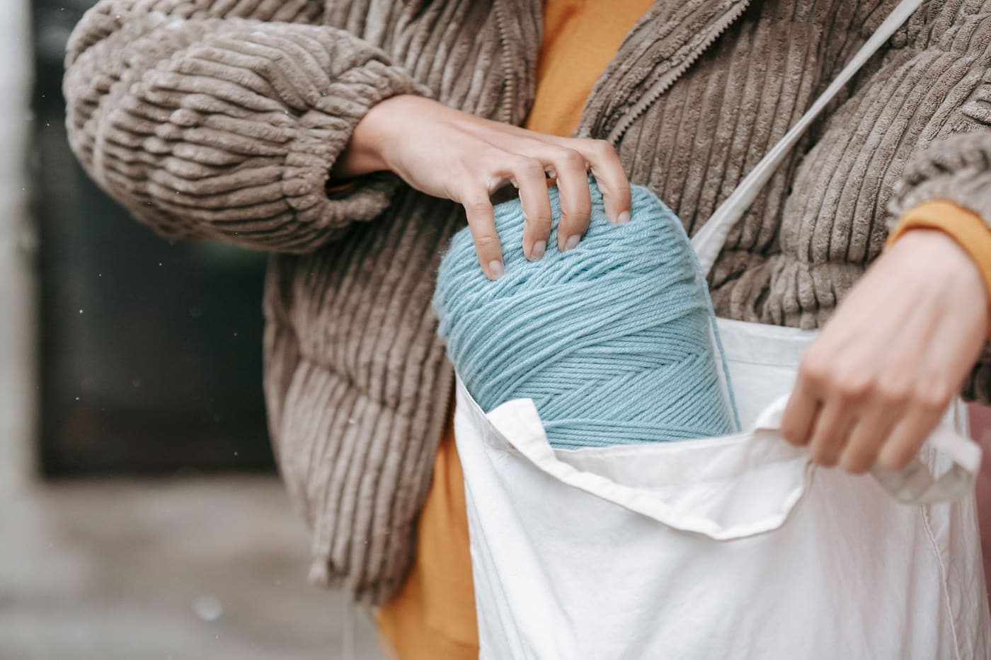 A person putting a skein of yarn into a cloth tote bag outdoors