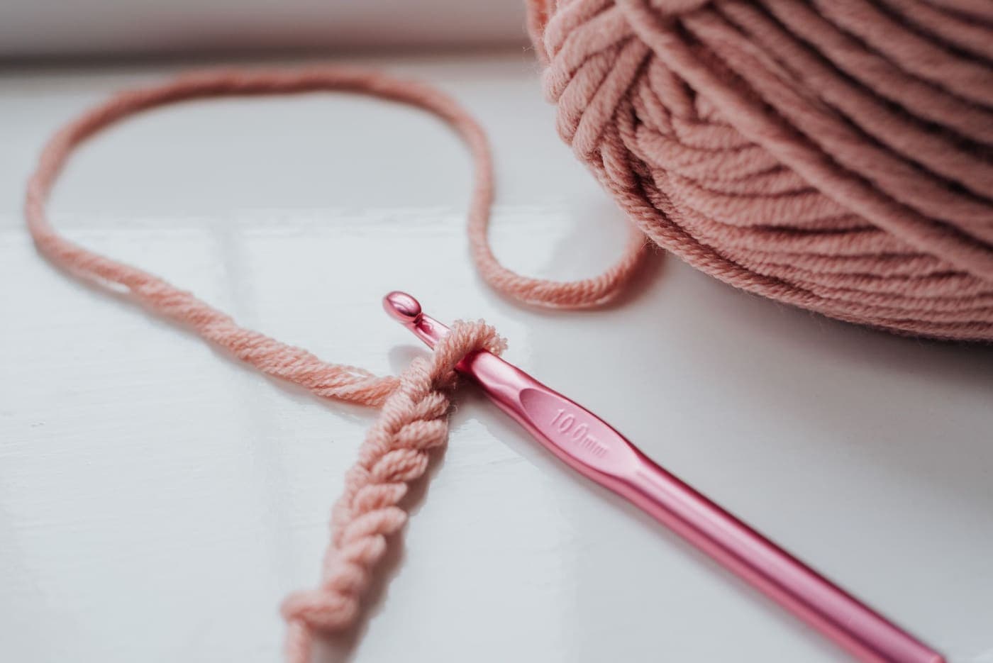 A small knitted piece with a shiny crochet hook and yarn on a windowsill