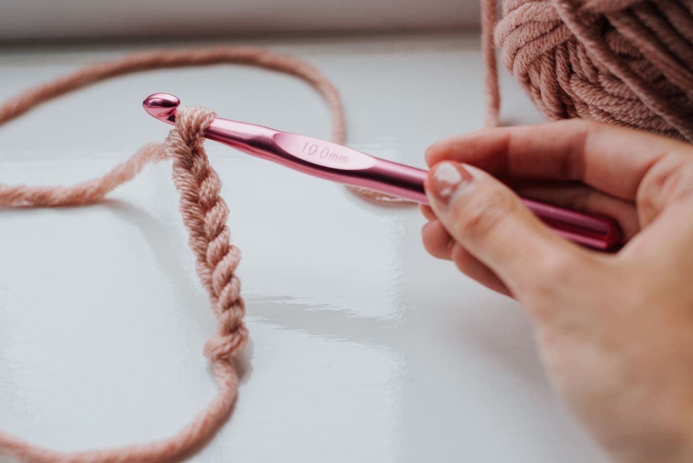 A person working a row of loops with a crochet hook in daylight