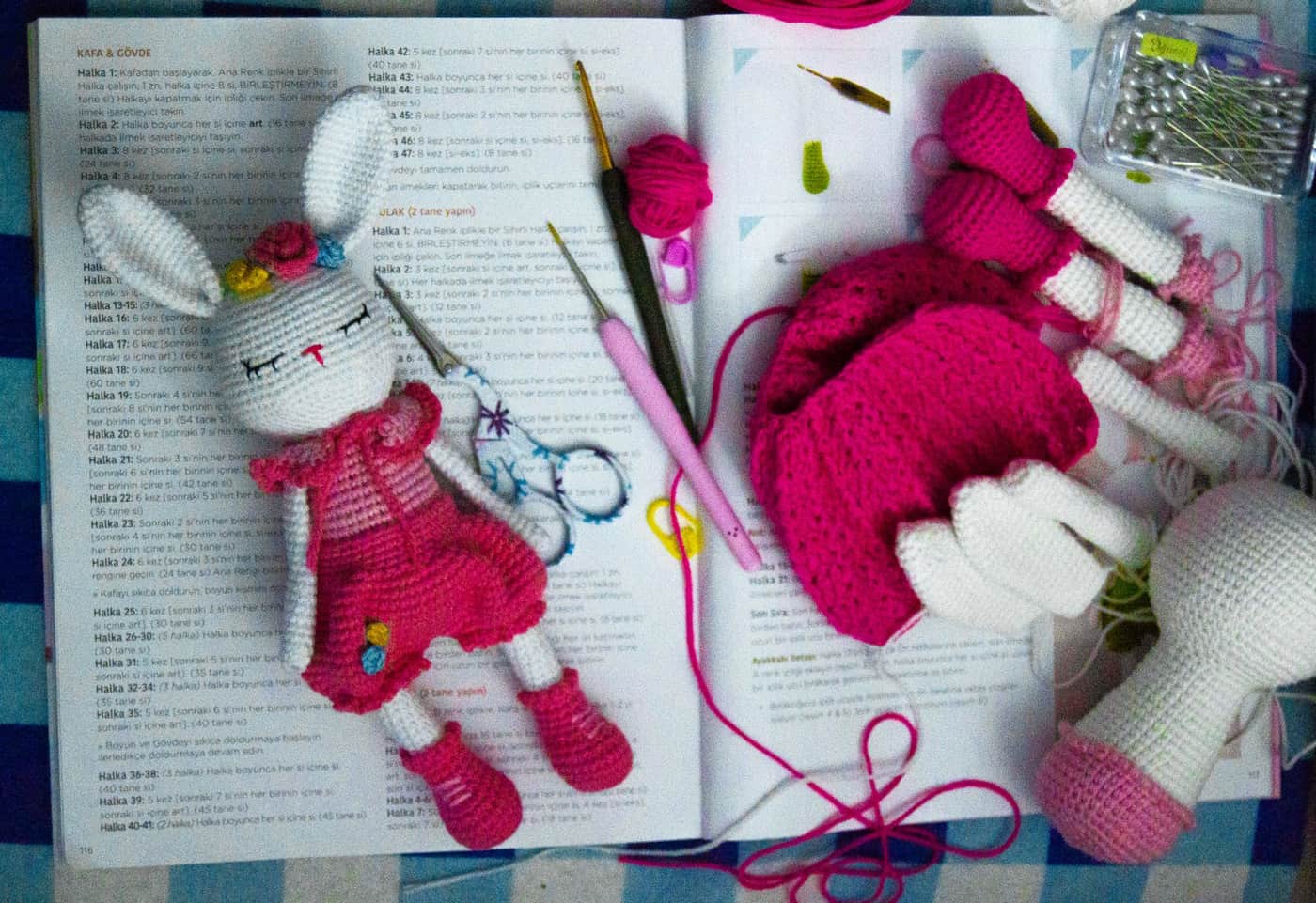 A handmade crochet bunny toy with crochet tools resting on a crochet handbook