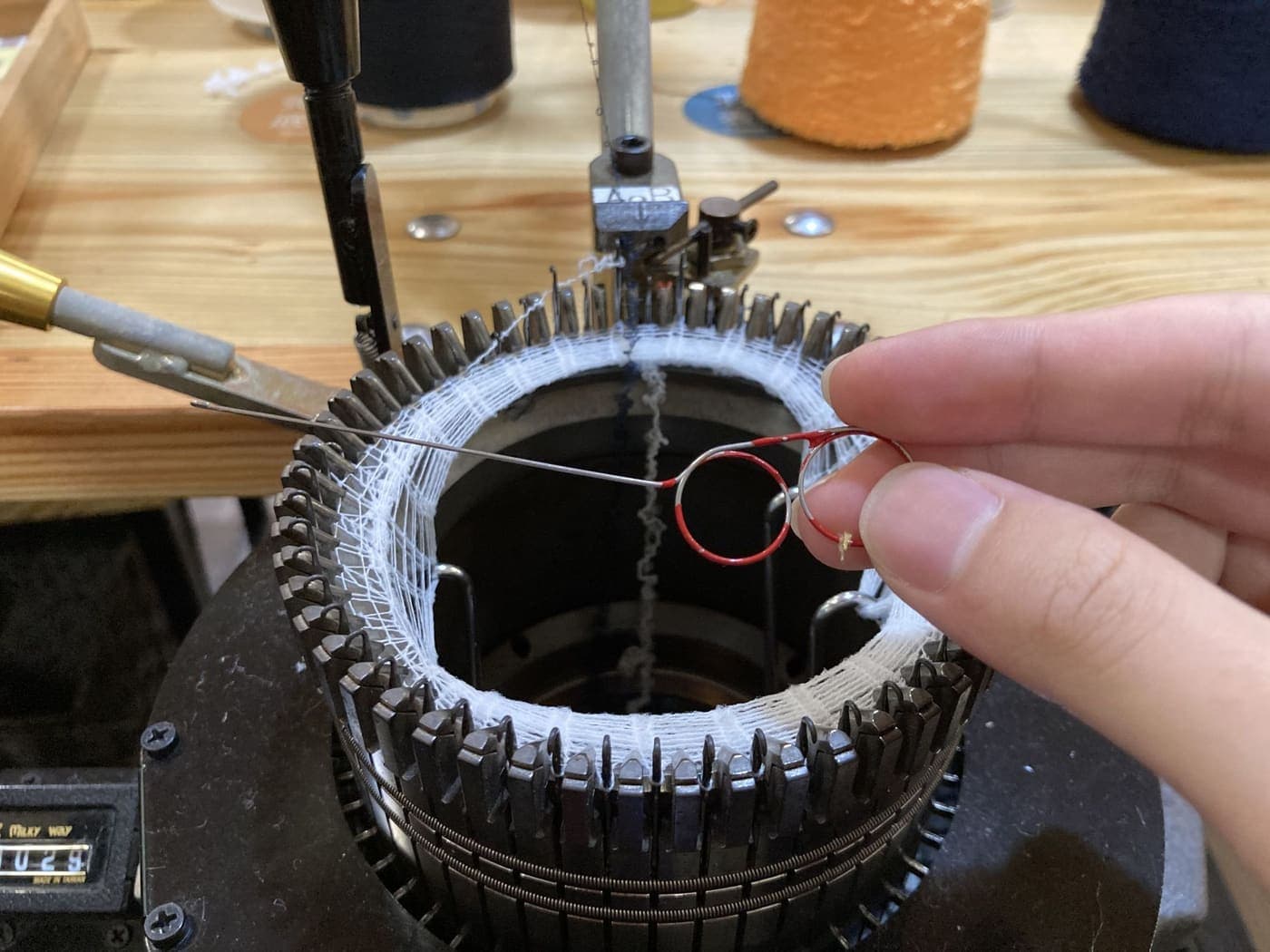 A hand threading yarn into a knitting machine