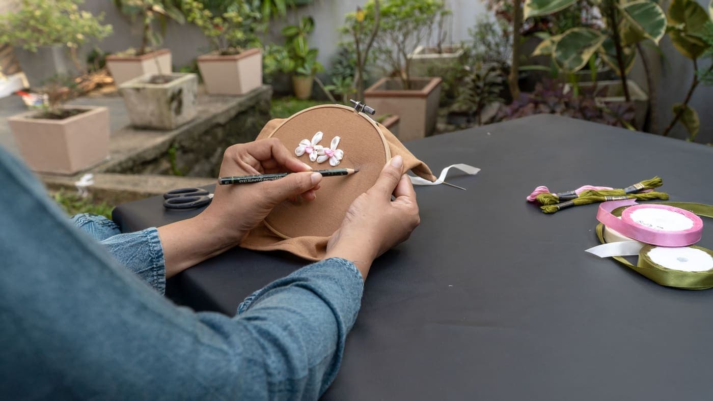 Hands working on fabric stretched in an embroidery hoop at an outdoor table
