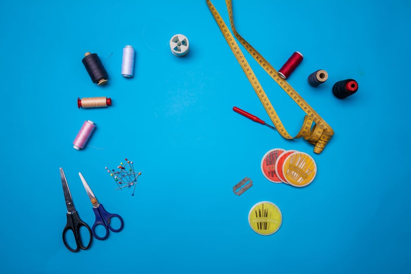 A flat lay of craft supplies including threads and scissors on a blue background