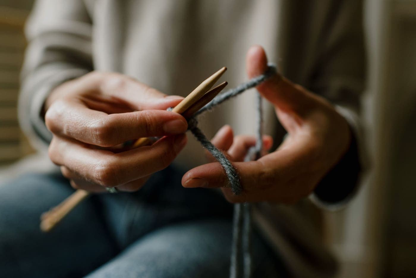 Hands knitting with wooden needles and gray yarn