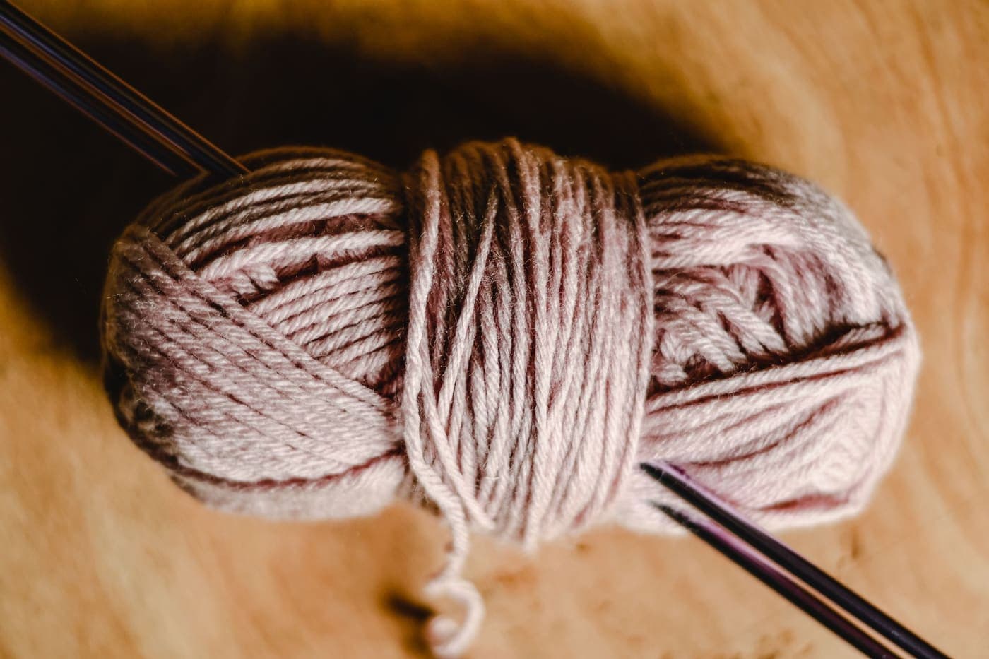 A skein of yarn with knitting needles resting on a wooden surface