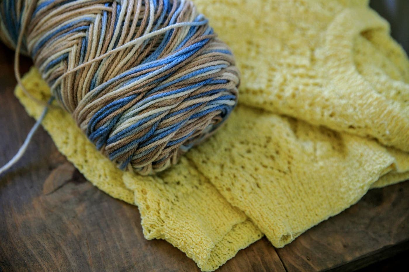 A ball of colorful wool yarn beside a knitted yellow sweater