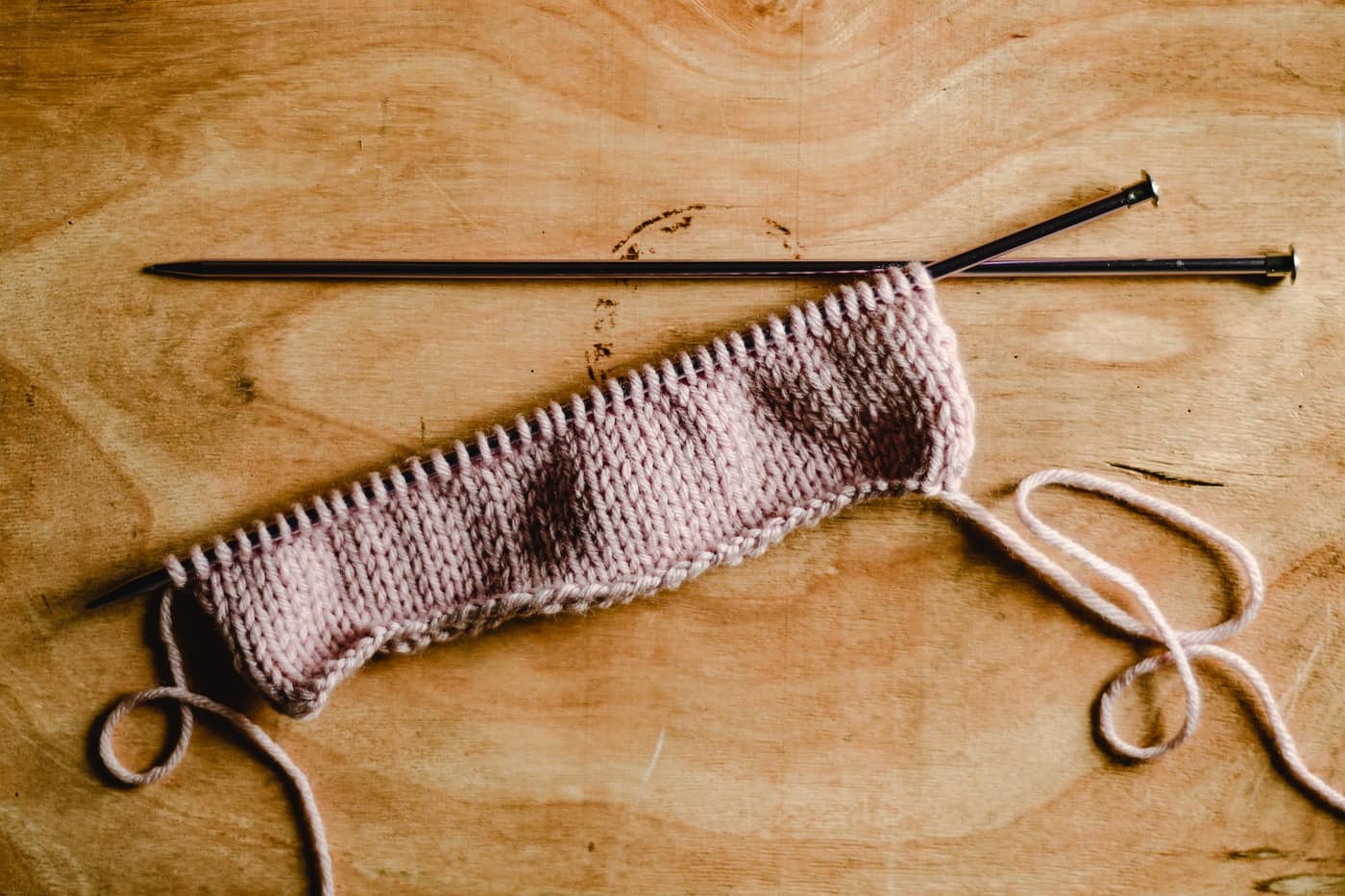 Double pointed knitting needles and a ball of pink yarn on a wooden table