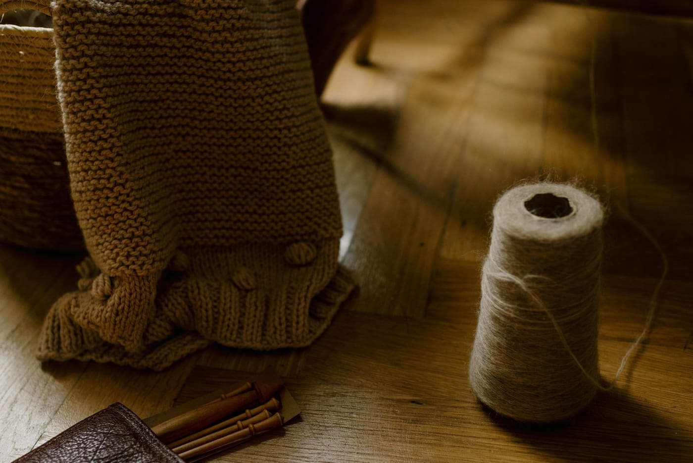 A handmade knitted blanket in a wicker basket beside wooden knitting needles