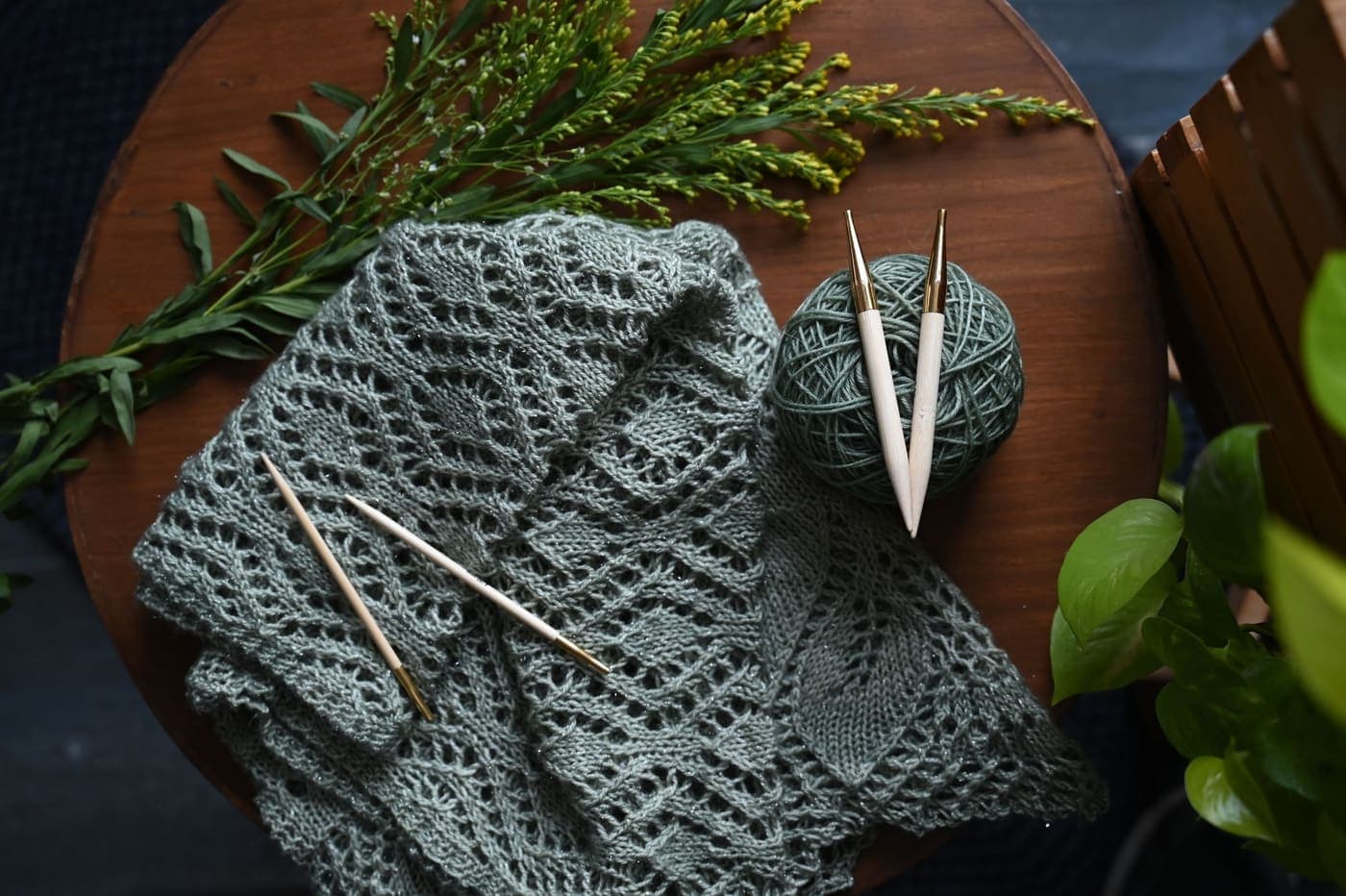 An openwork knitted shawl and hooks laid on a wooden table with foliage
