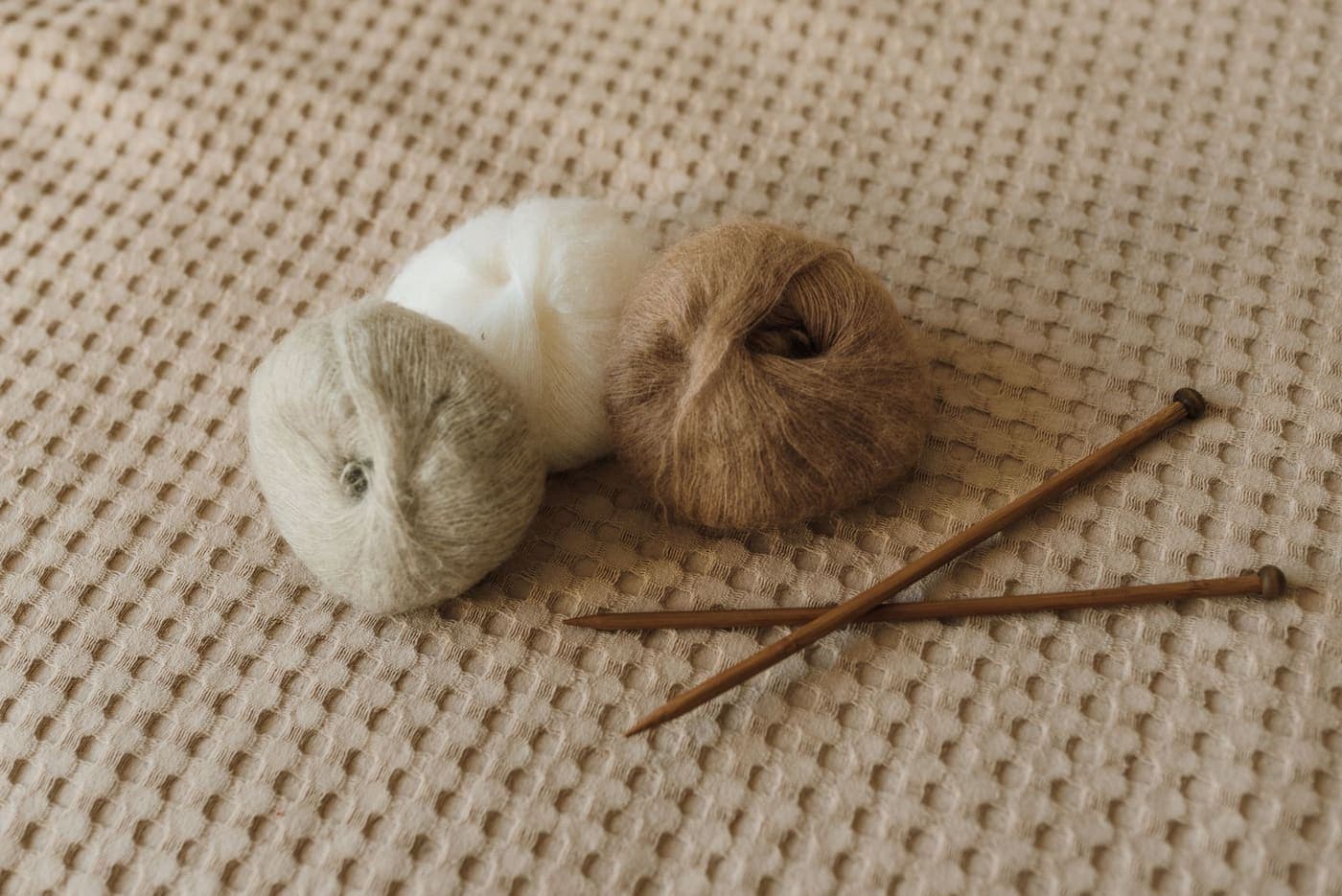 Yarn rolls and knitting needles on a textured fabric surface