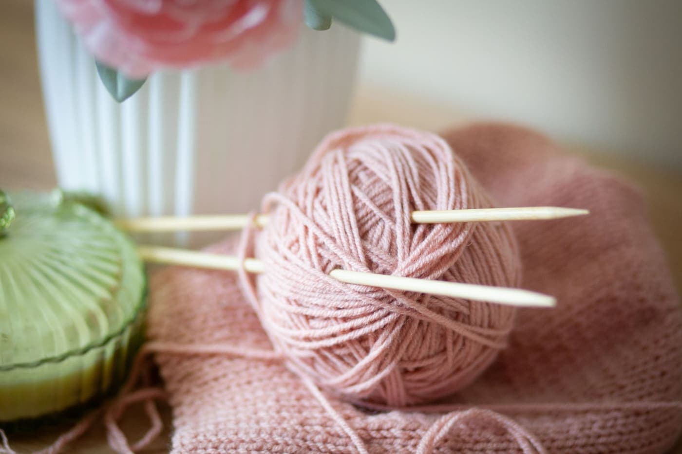 A pair of knitting needles resting against a ball of pale pink yarn