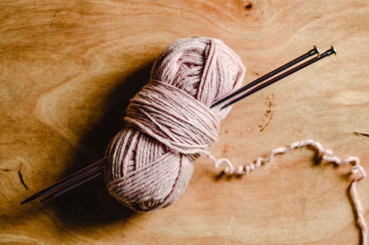 A ball of yarn and knitting needles resting on a wooden table
