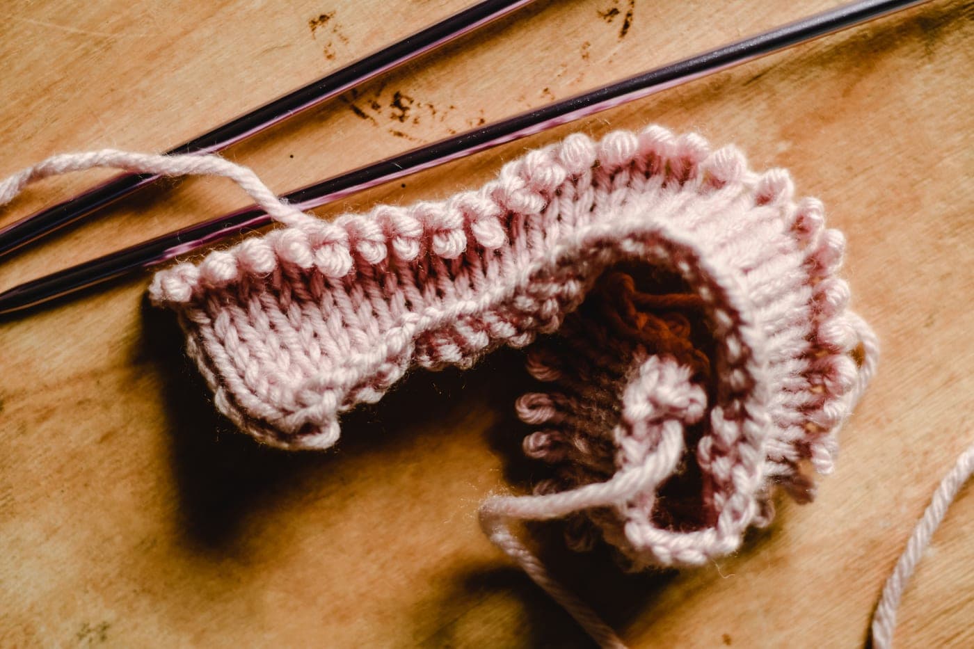 A row of knitting needles of increasing diameter arranged on a light background