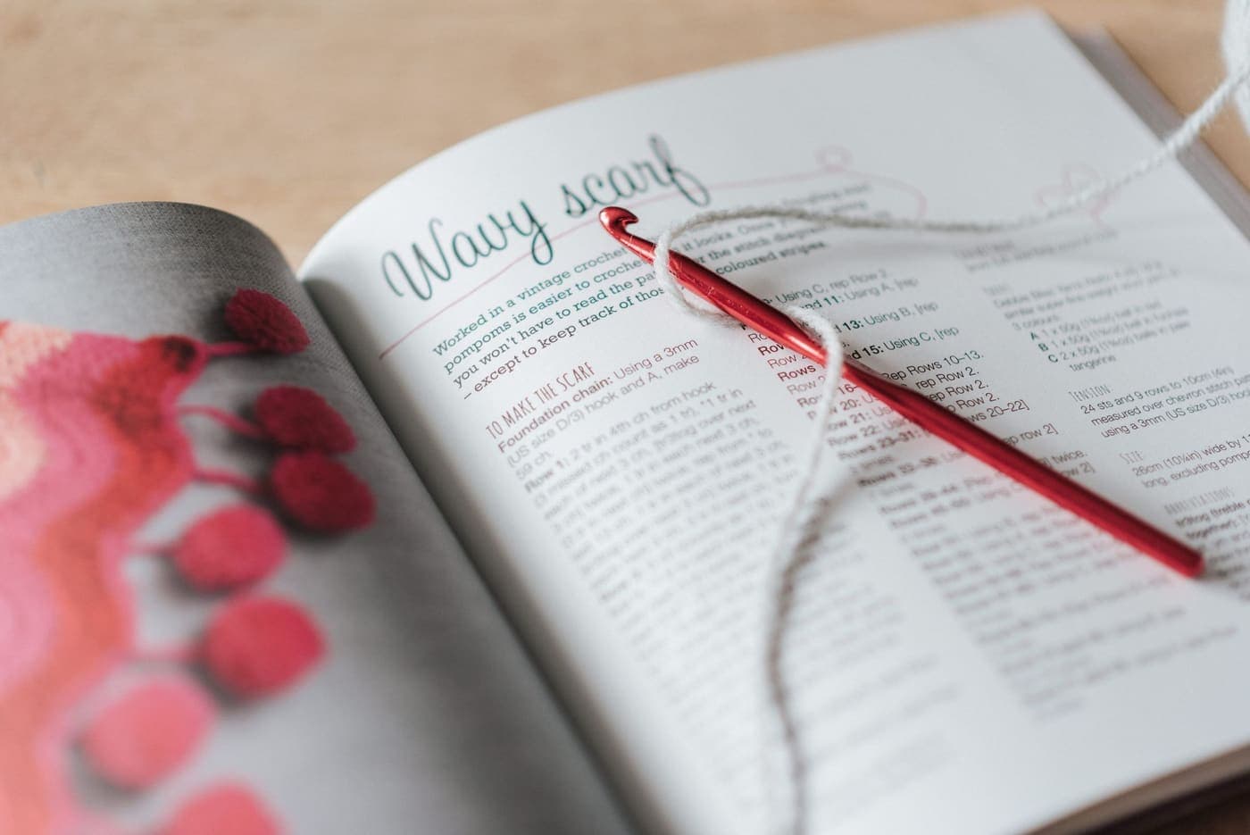 A red crochet hook and gray thread resting on an open magazine
