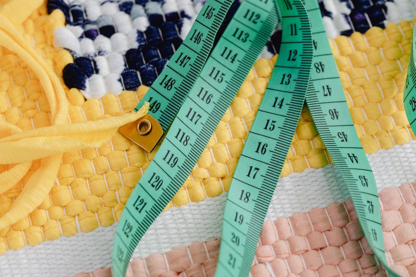 A green measuring tape lying on a colorful woven textile
