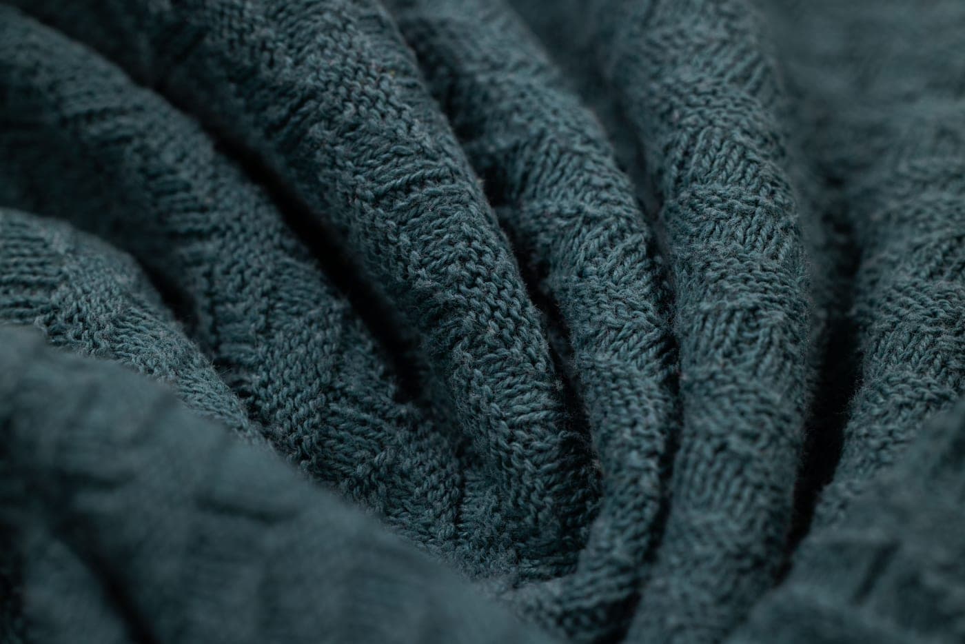 A soft knitted baby blanket folded on a plain surface with yarn alongside