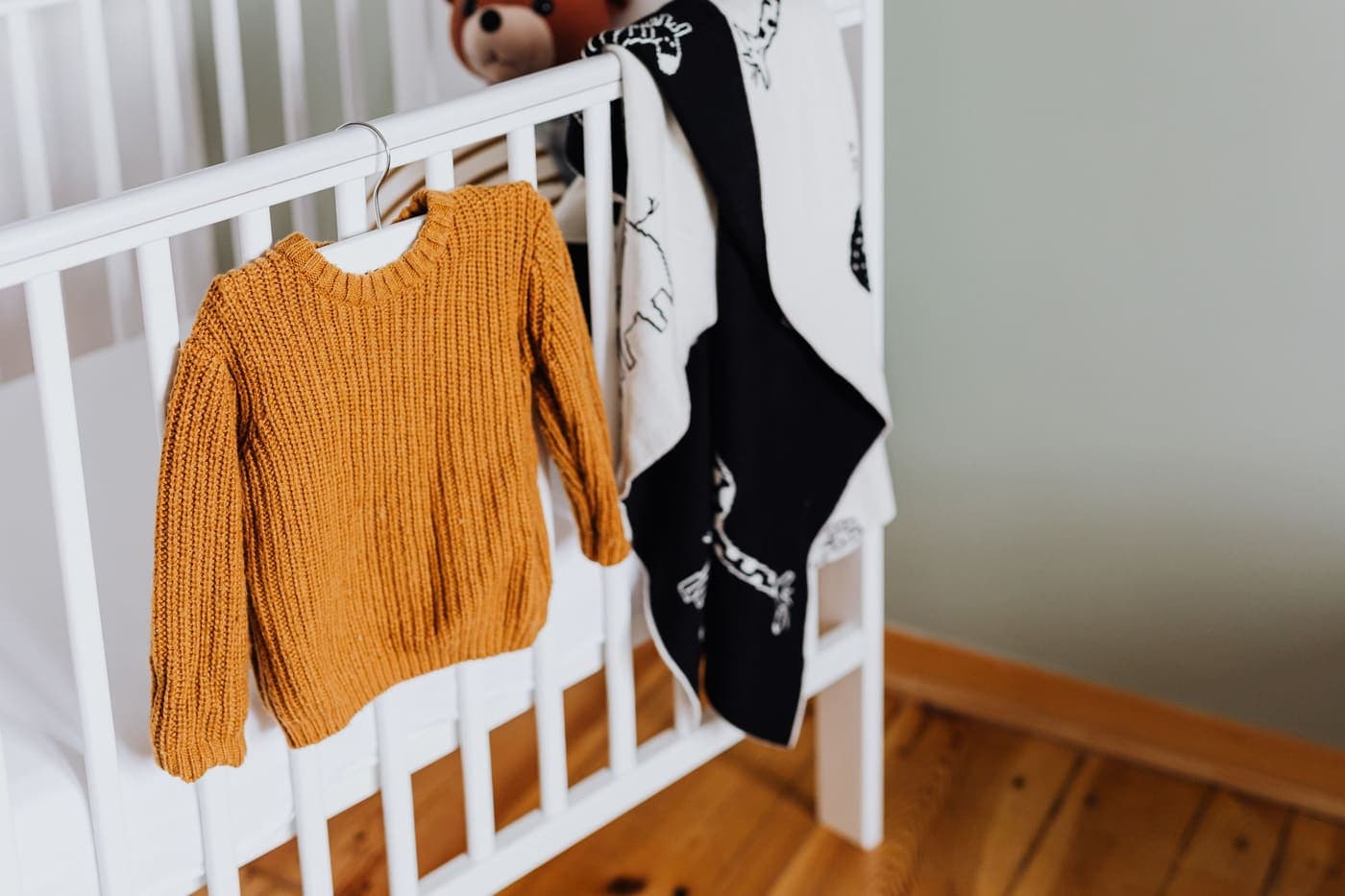 A mustard knitted baby sweater hanging on a white crib