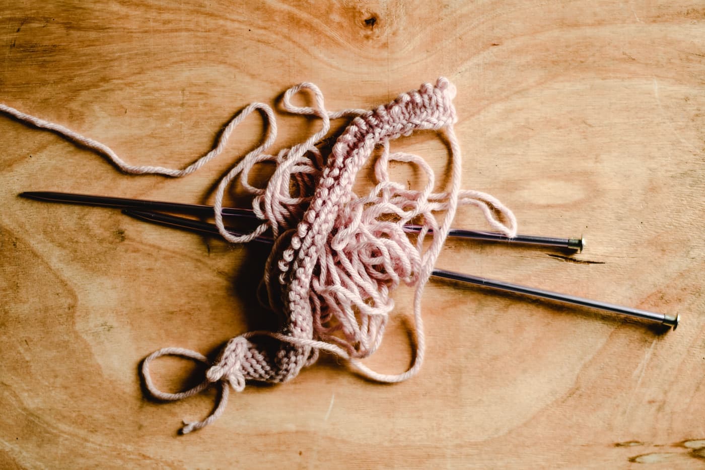 A ball of smooth light-colored worsted yarn beside a beginner knitted swatch