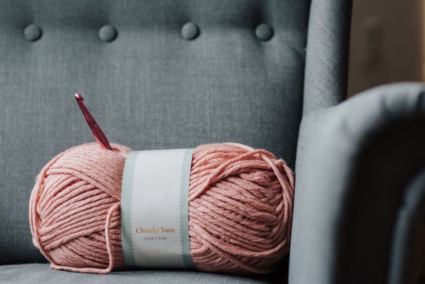 Soft pink yarn and a crochet hook resting on a gray couch