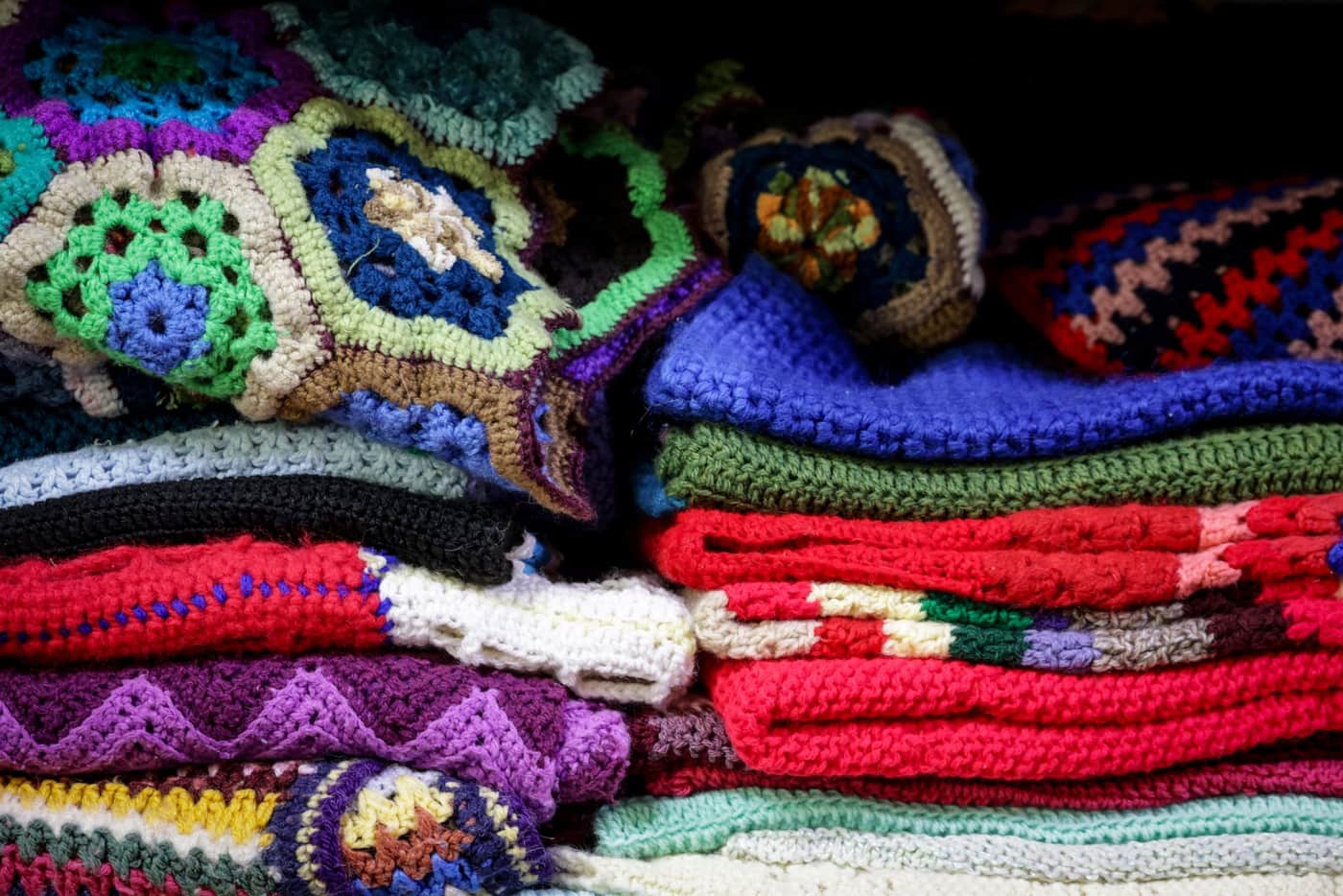 A stack of colorful vintage crochet blankets with intricate patterns