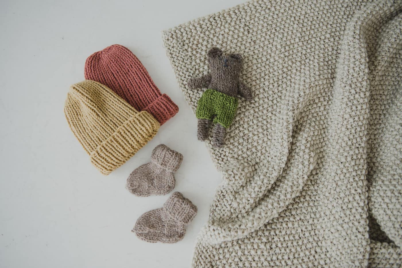 Knitted beanies and a small toy bear arranged on a white surface
