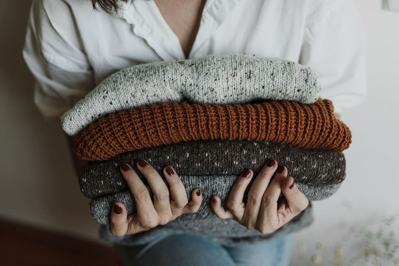 A person holding a stack of folded knitted garments in various colors