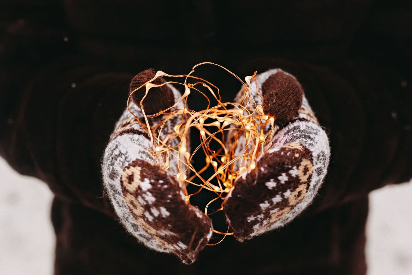 Hands in wool mittens holding a string of warm fairy lights